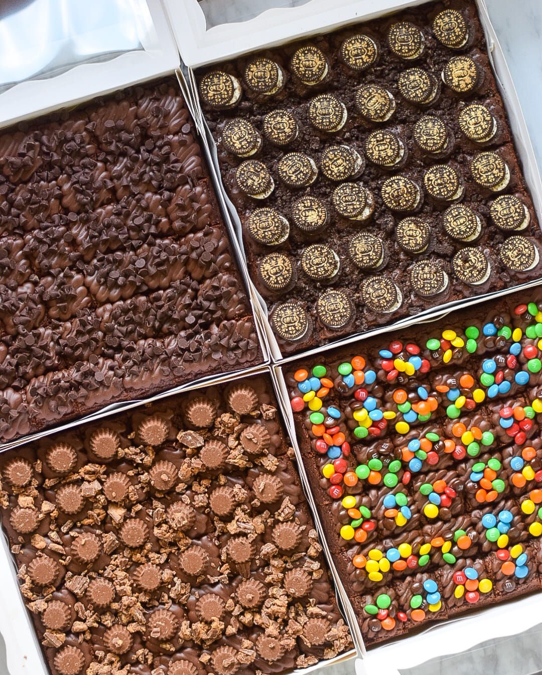 Four boxes of brownies with different toppings are sitting on a table.