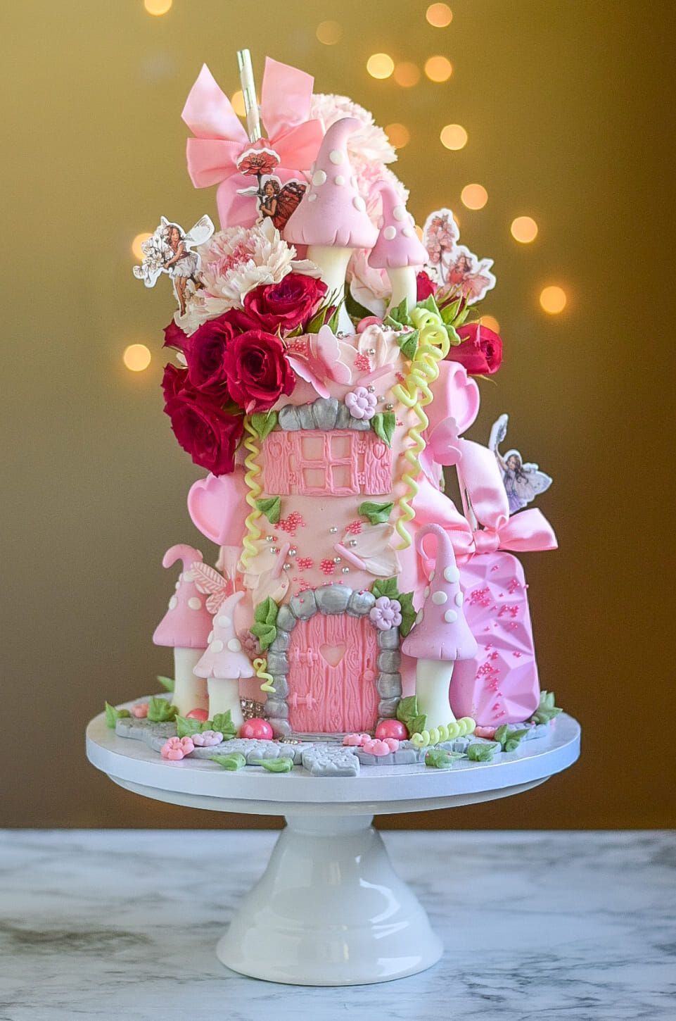 A pink fairy castle cake is sitting on a white cake stand.