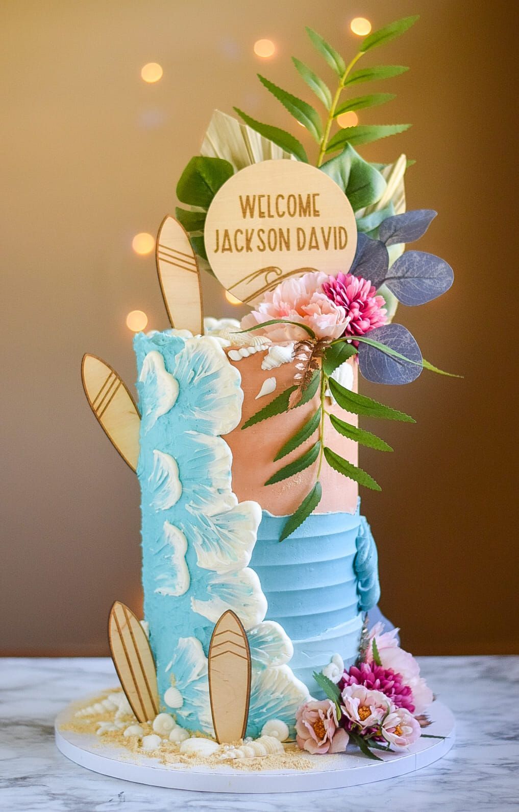 A cake with surfboards and flowers on it is on a table.