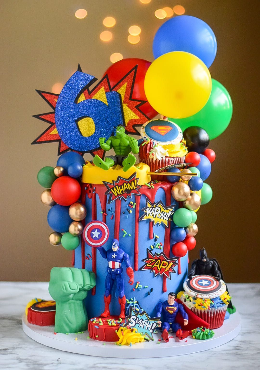 A cake decorated with superhero characters and balloons for a boy 's 6th birthday.