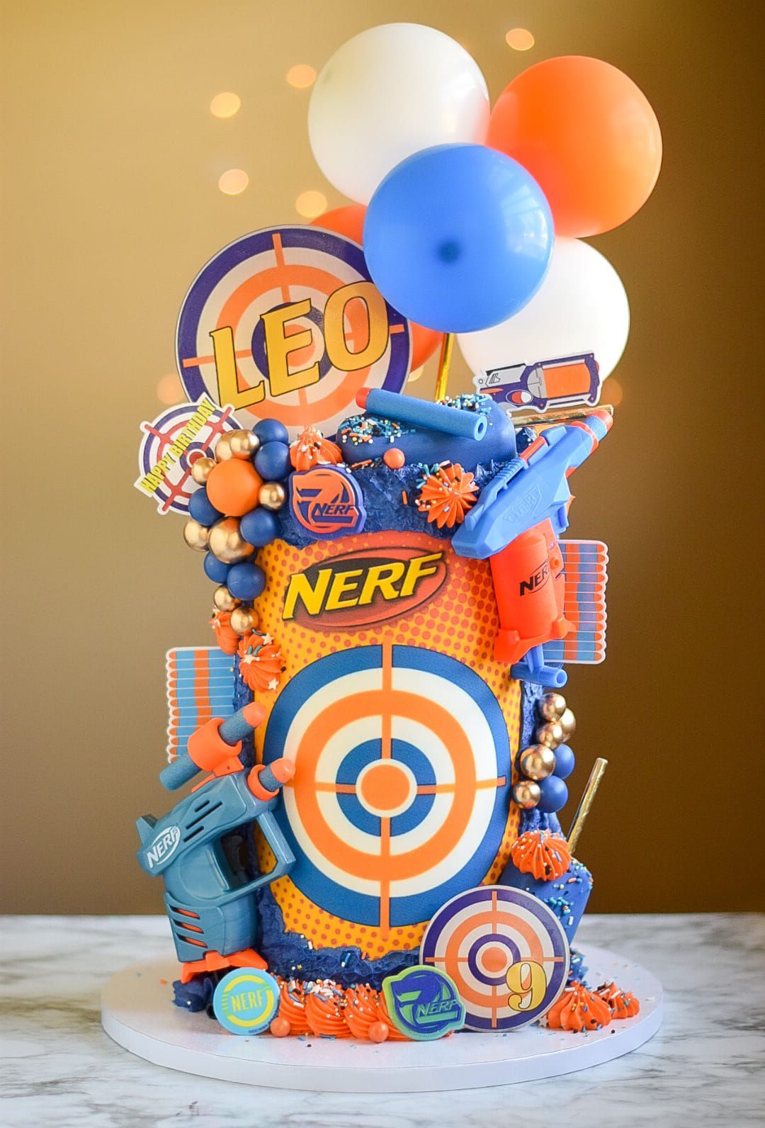 A nerf cake with balloons and candy on top of it.