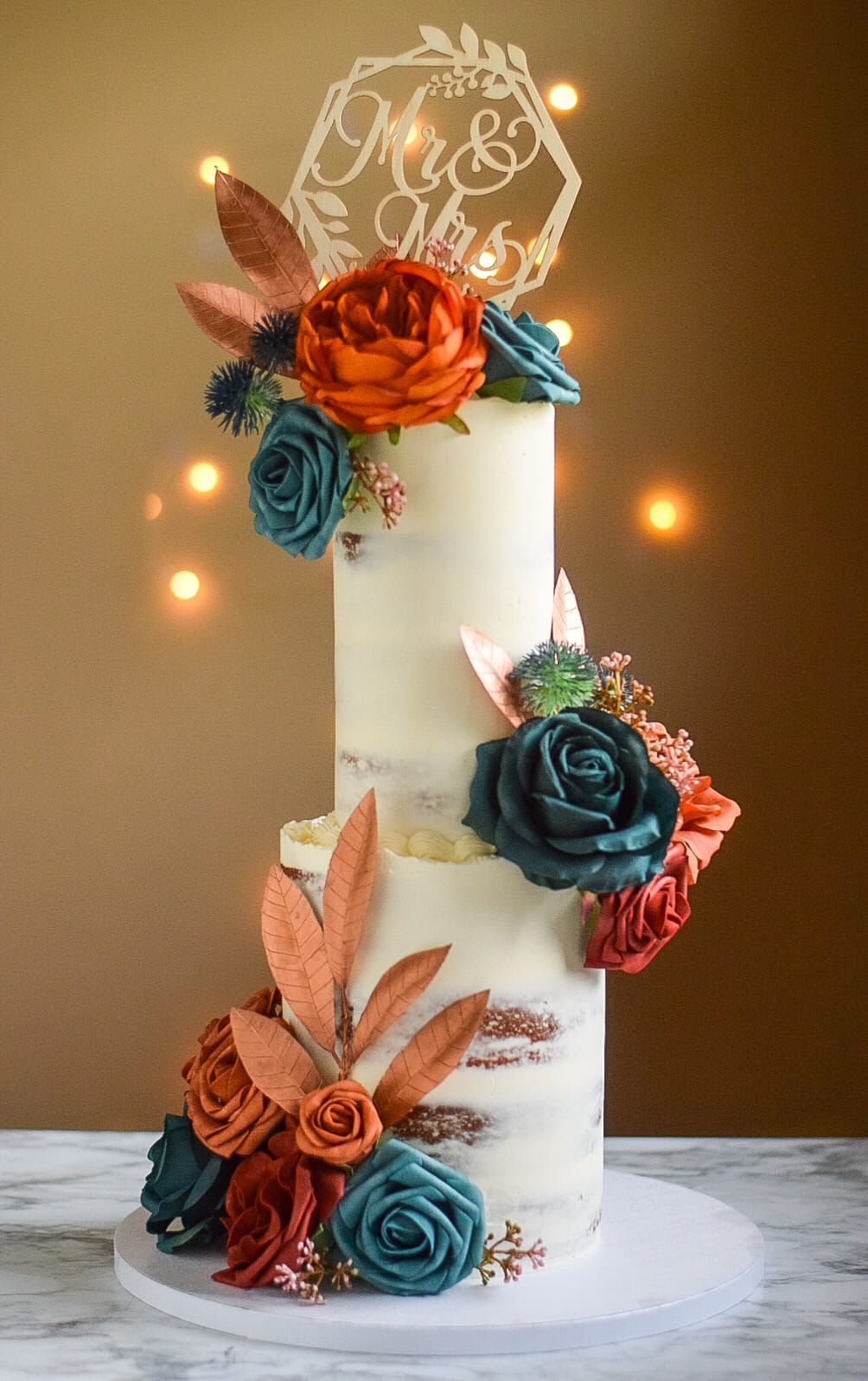 A wedding cake with flowers and leaves on it is sitting on a table.