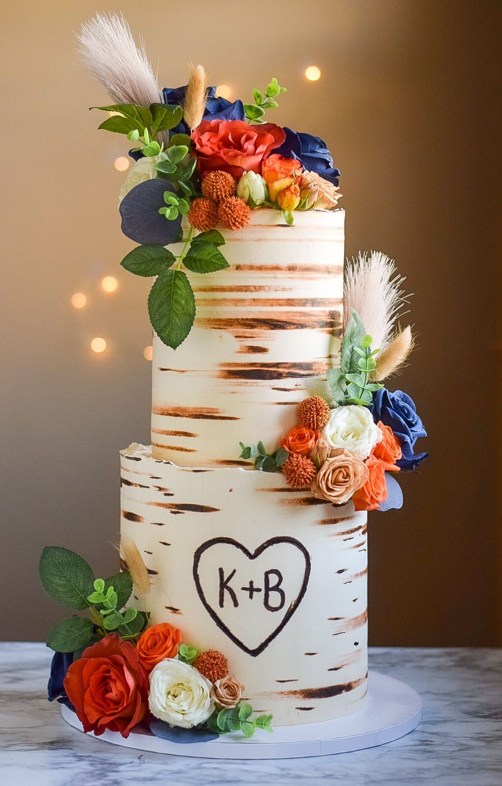 A three tiered wedding cake decorated with flowers and feathers on a table.