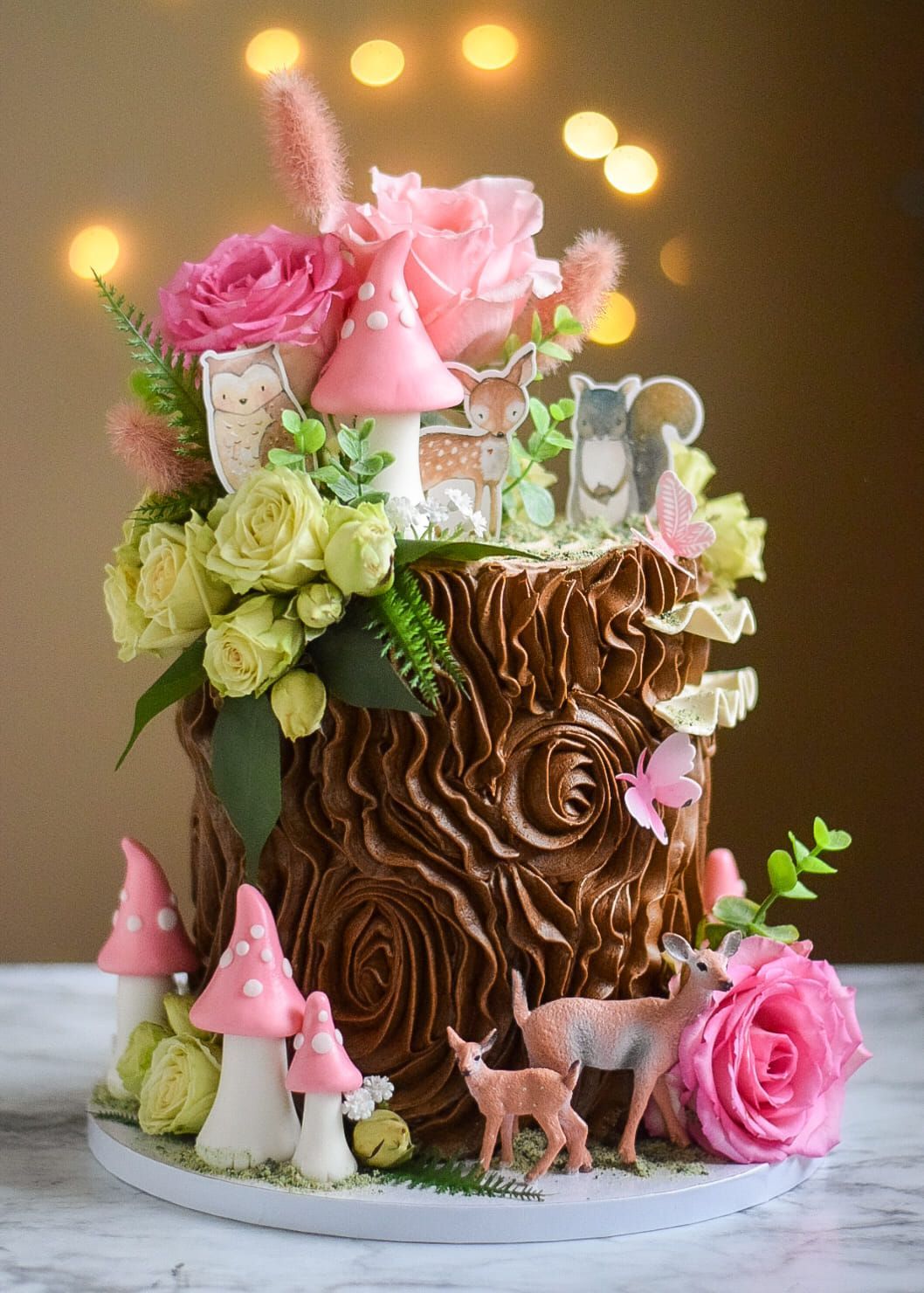 A cake decorated to look like a tree stump with flowers and mushrooms on top.