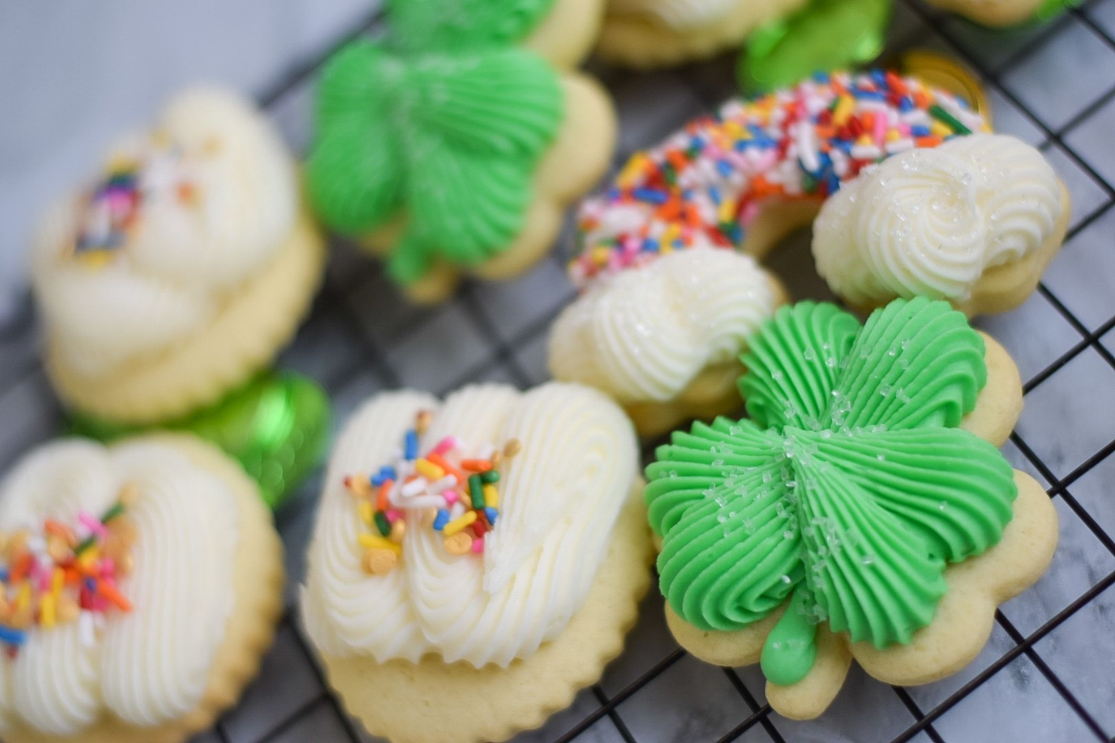 Cookies decorated with green frosting shamrocks, rainbow sprinkles, and white frosting.