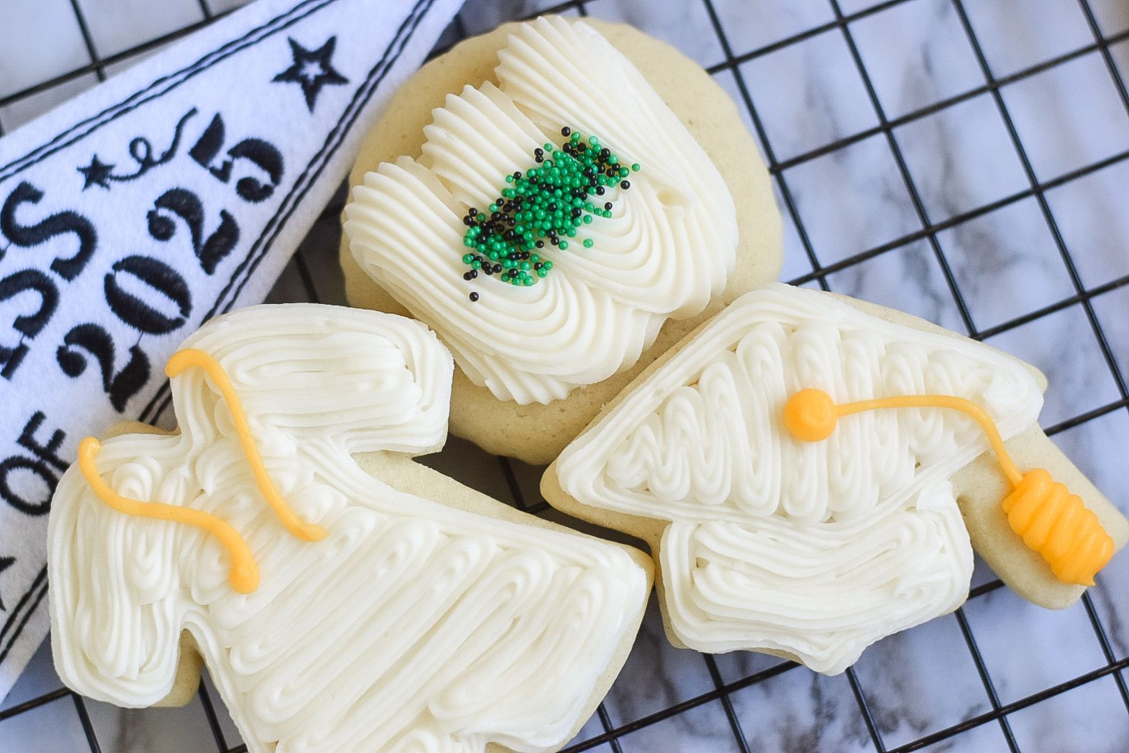 Graduation cookies decorated as cap, gown, and diploma, with white frosting and yellow and green details.
