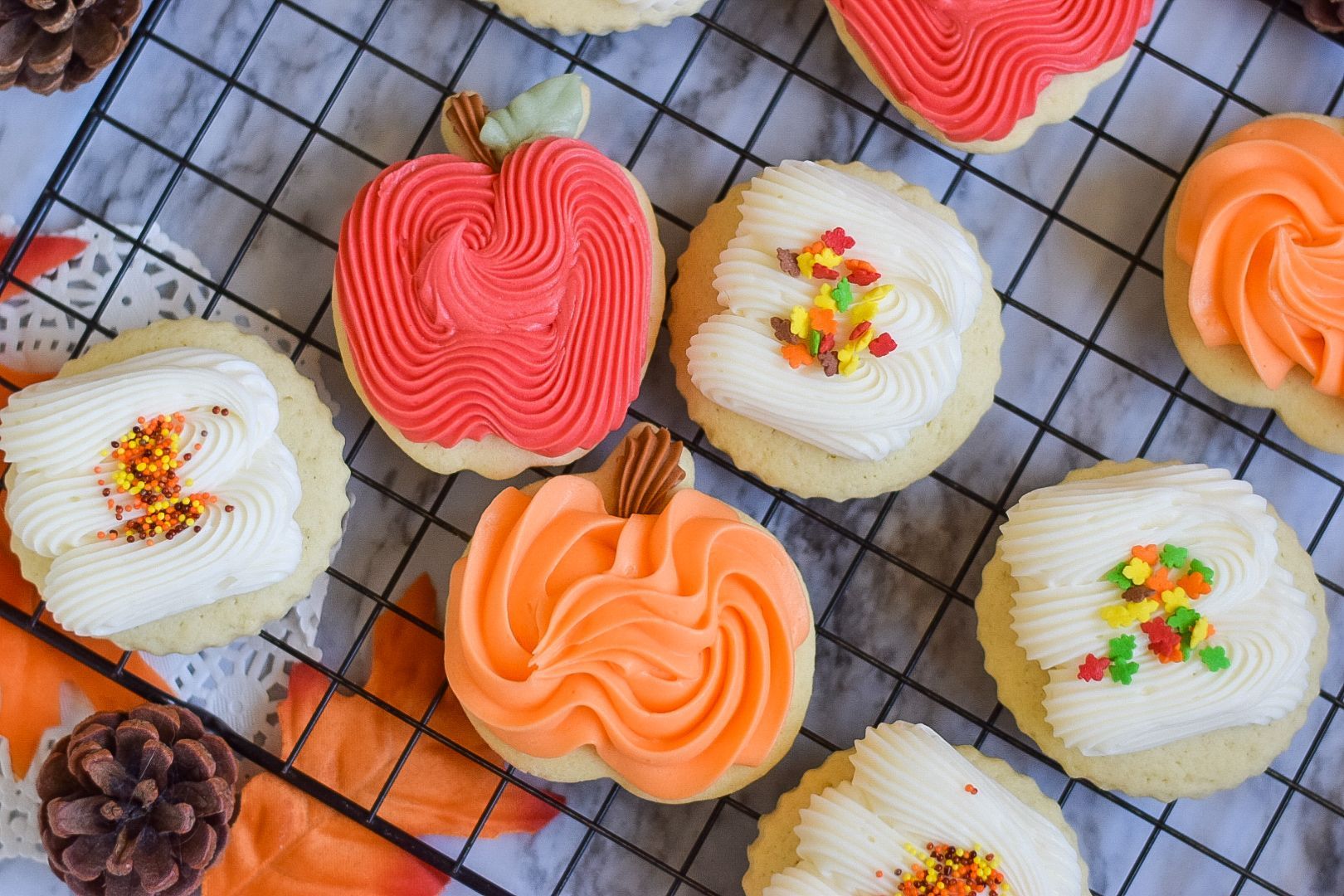 Autumn-themed frosted sugar cookies: apple, pumpkin, and round shapes, decorated with colorful frosting and sprinkles.