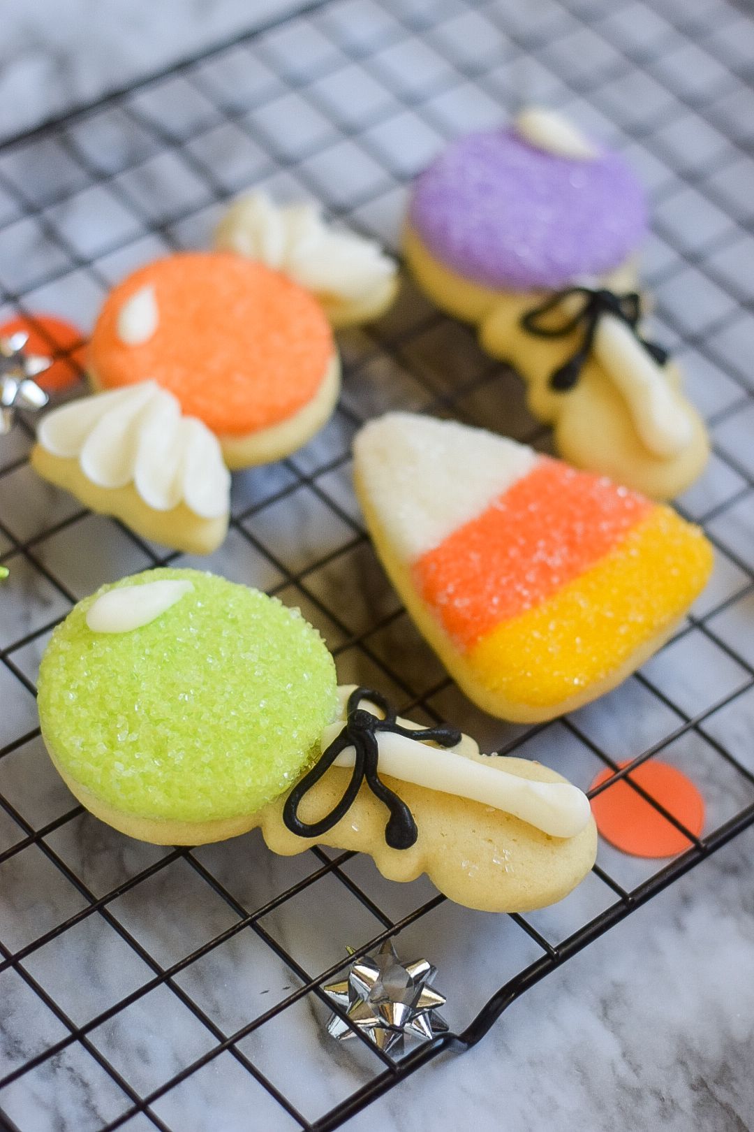 Halloween cookies on a wire rack: orange, purple, green, and candy corn shapes, frosted and sprinkled.