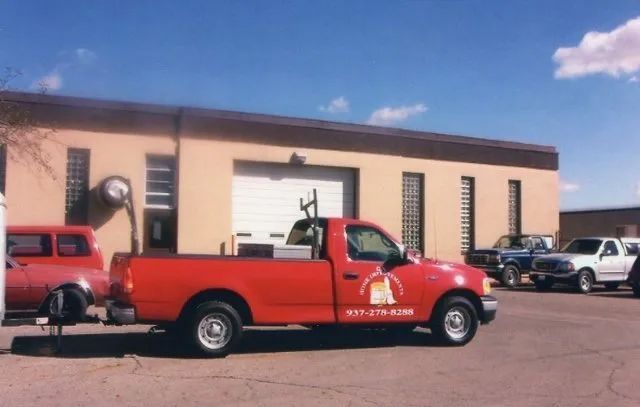 Red tow truck parked in front of a beige garage building under a blue sky