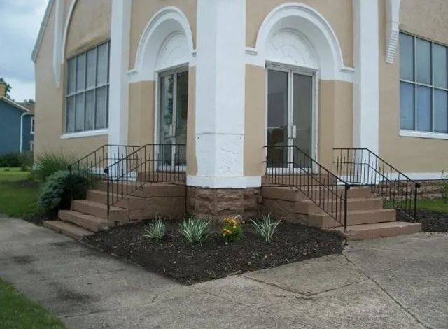 Front entrance of a building with twin stairways, black railings, and arched white columns.