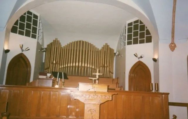 Church sanctuary with wooden altar, organ pipes, and arched windows behind the pulpit.