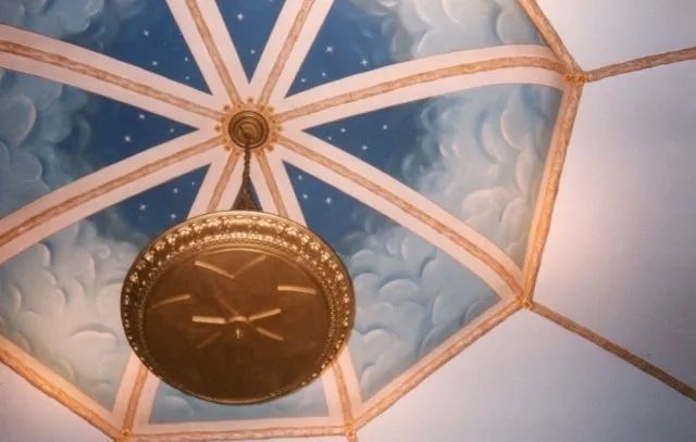 Blue ceiling with white spokes and a central brass clock, viewed from below