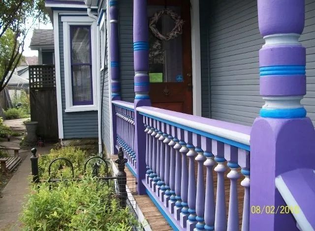 Purple-painted porch railing and columns beside a house entrance, with a garden path on the left.