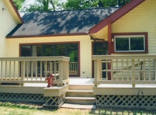 Yellow house with a wooden front deck, steps, and railing under a shaded roof.