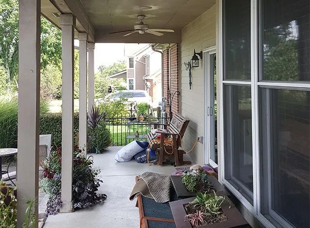 Covered front porch with chairs, potted plants, and a ceiling fan overlooking a suburban street