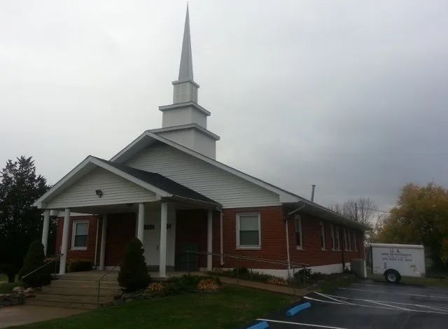 Brick church with white steeple and porch on a cloudy day