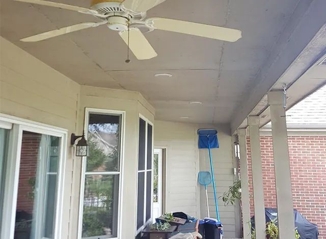 Covered porch with white ceiling fan, windows, and a ladder leaning against the wall.