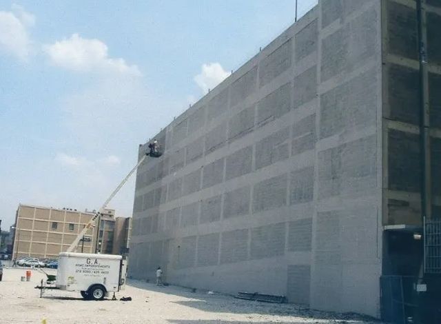 Large gray industrial building under construction with a boom lift and utility truck on a paved site