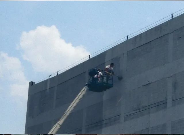 People in a suspended basket work on the side of a tall concrete building.