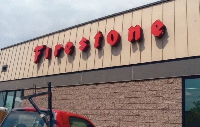 Firestone store sign on a beige building with part of a red truck visible below