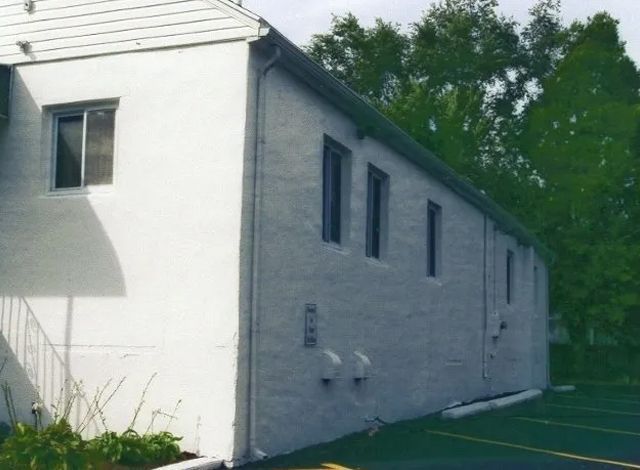 White brick building exterior beside a paved lot and trees