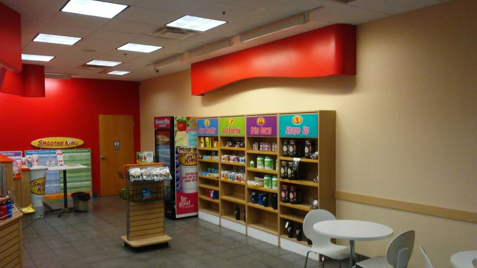 Empty store interior with red walls, display shelves, and a small seating area under bright ceiling lights