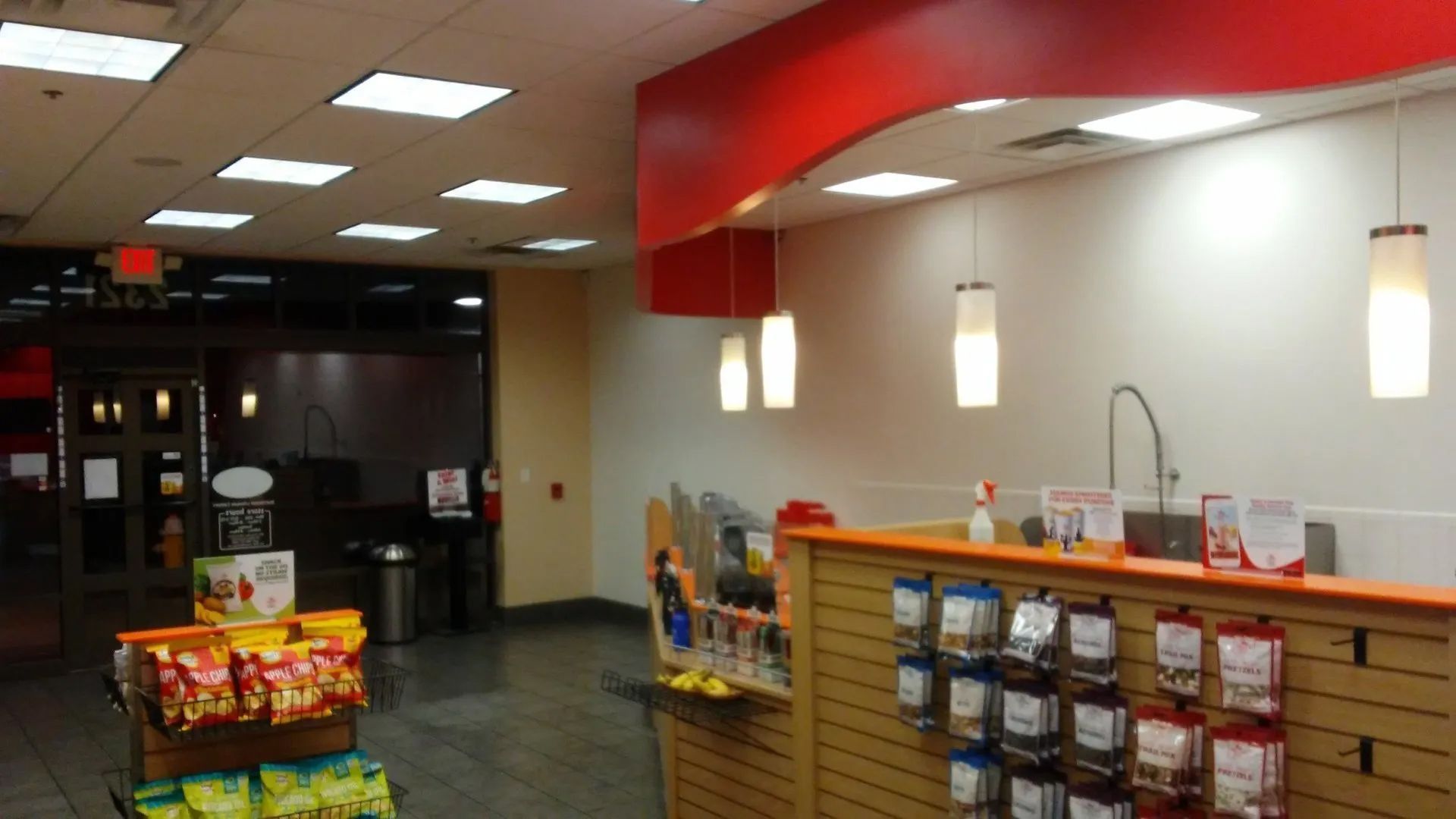 Convenience store interior with snack shelves, beverage display, and cash register counter under bright lights