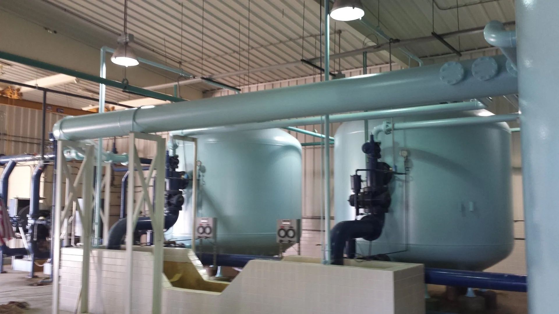 Large industrial tanks and pipes in a mechanical room with workers in the background