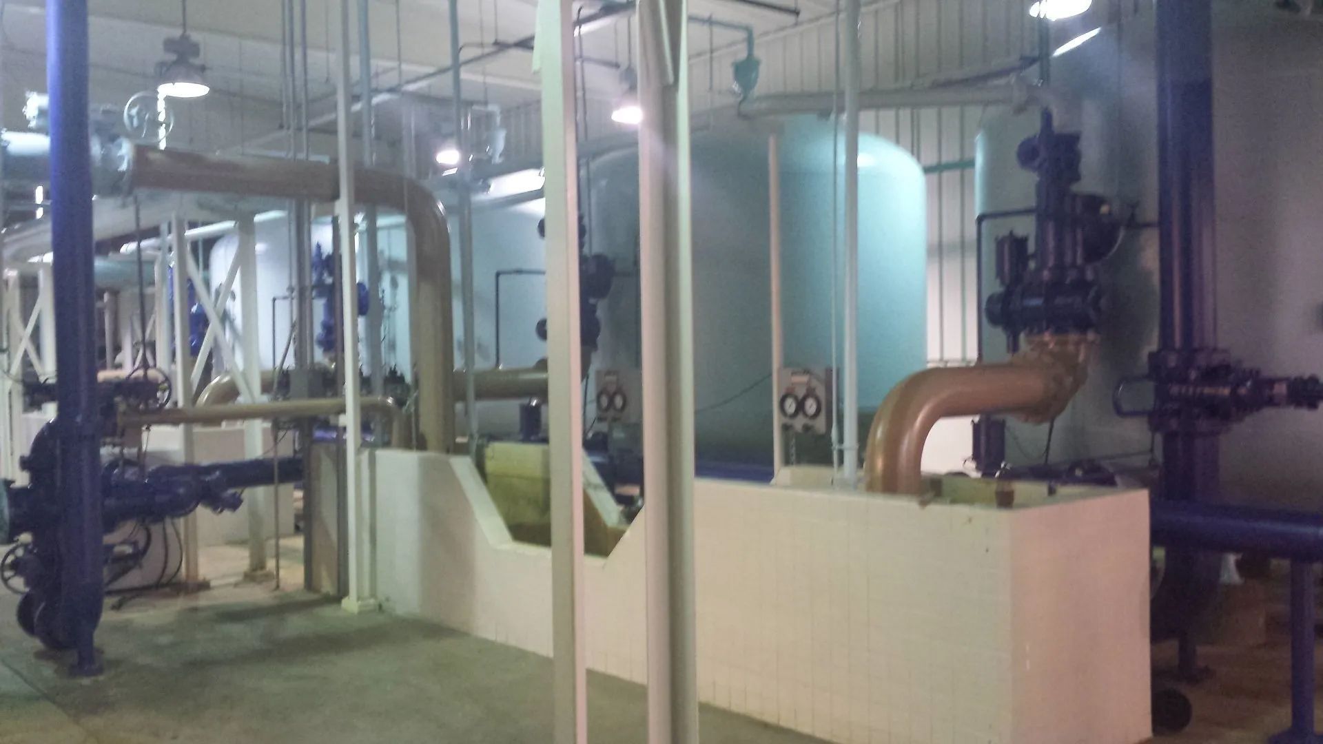 Industrial machinery in a factory room with blue pipes, tanks, and white equipment partitions