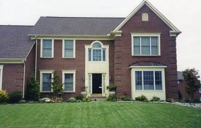 Suburban two-story brick house with dark roof and manicured green lawn