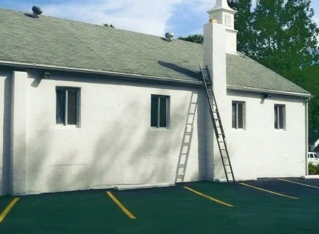 White building with two ladders leaning against the roof in a parking lot