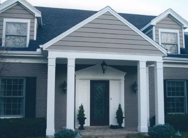 Front view of a gray house with white trim, a gabled porch, and two potted shrubs at the entrance