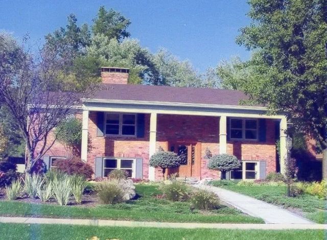 Brick suburban house with white trim, central walkway, and manicured front lawn under blue sky