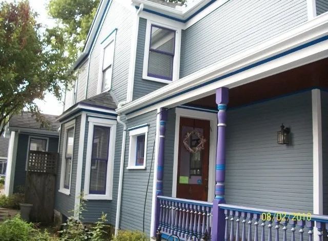 Gray house exterior with purple porch posts and railing, viewed from the side