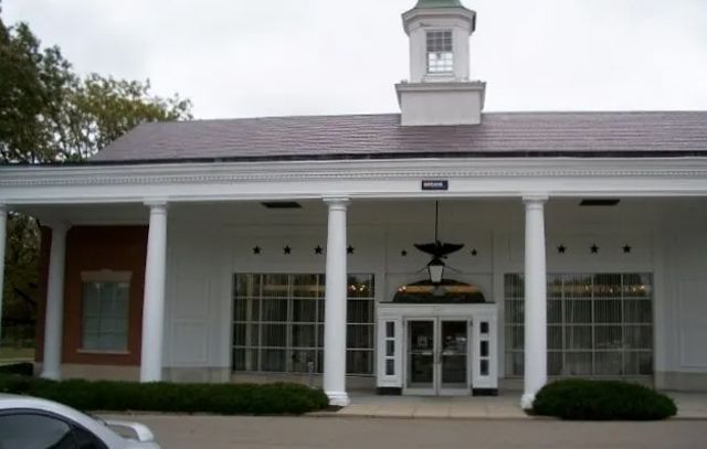 Front entrance of a building with white columns, a cupola, and glass doors under a dark roof
