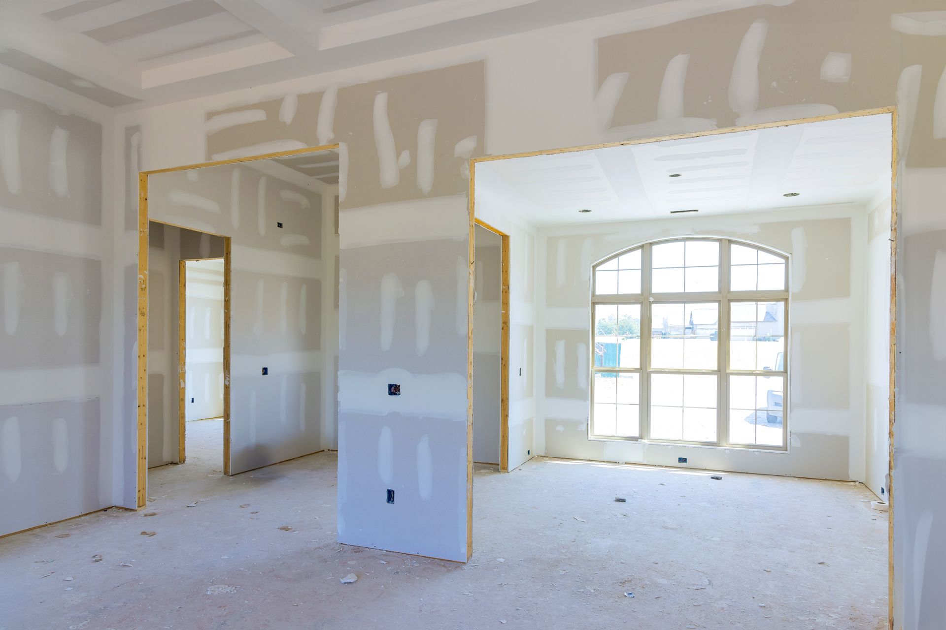 Unfinished room with drywall, exposed trim, and large arched window letting in bright light.