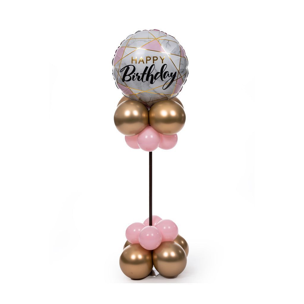 A happy birthday balloon surrounded by pink and gold balloons on a stand.