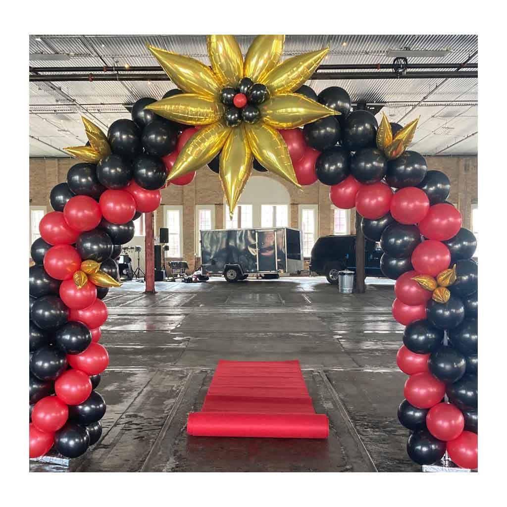 A red , black and gold balloon arch with a red carpet underneath it.