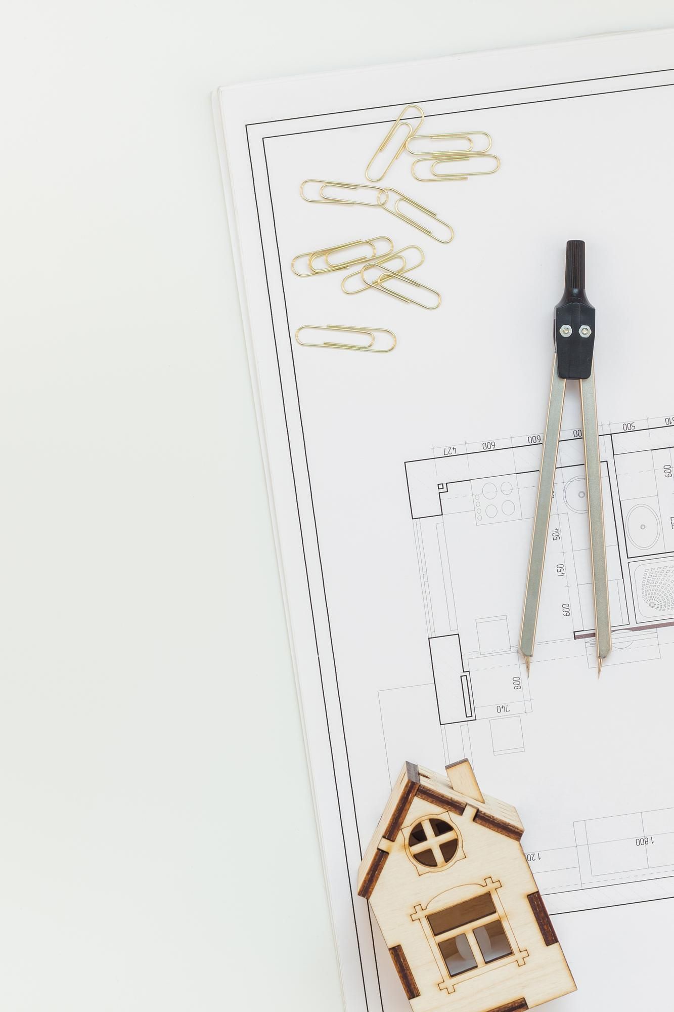 A small wooden house is sitting on top of a piece of paper next to a compass and paper clips.