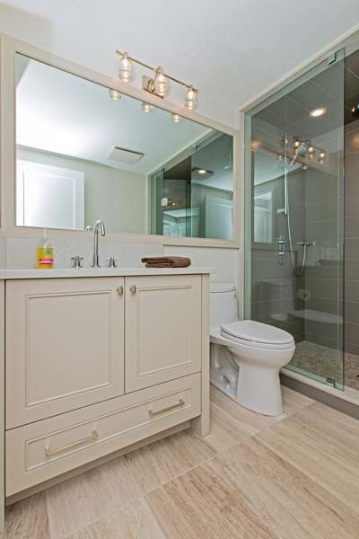 A bathroom with a toilet , sink , mirror and walk in shower.