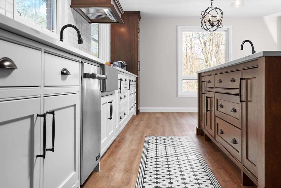A kitchen with white cabinets and wooden floors and a rug on the floor.