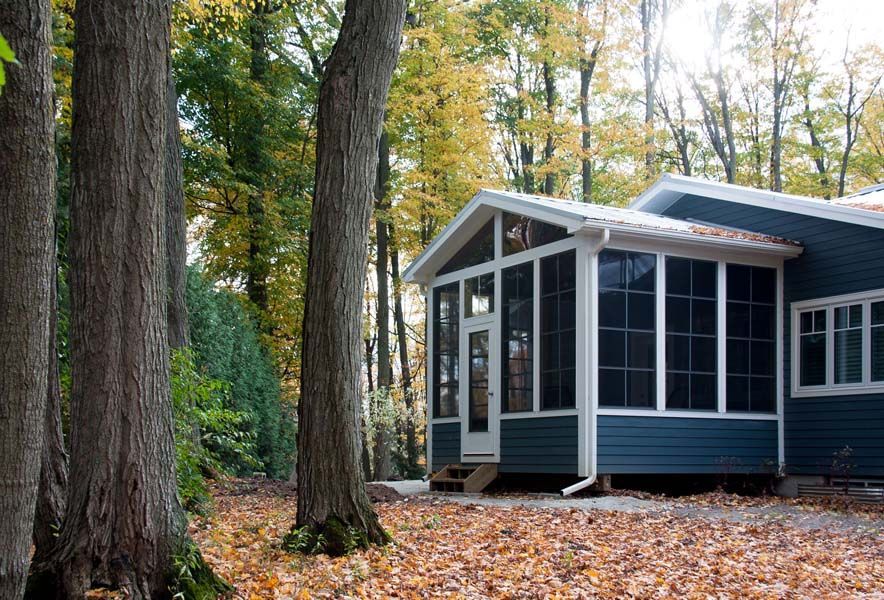 A house with a screened in porch in the middle of a forest.