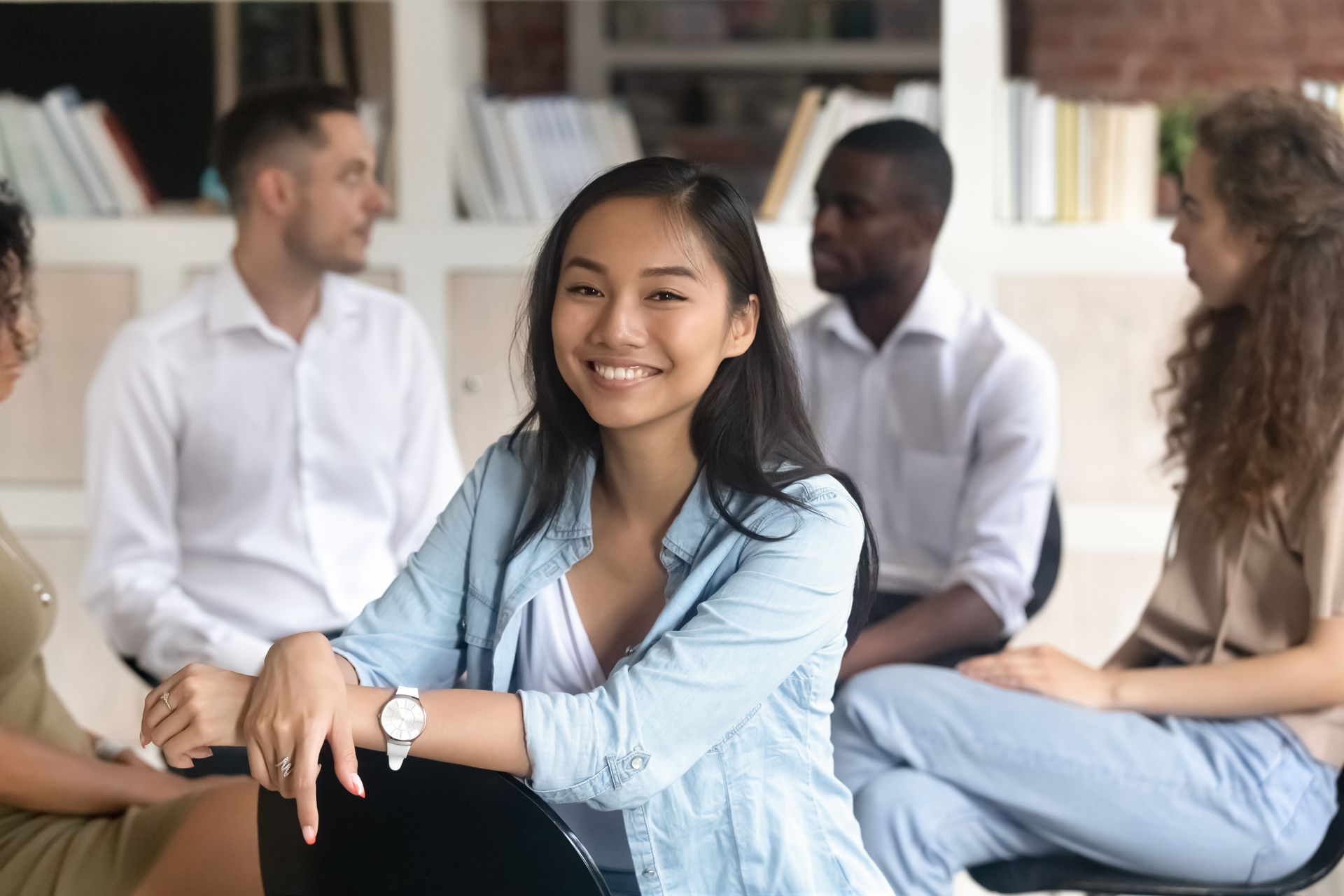 A woman is smiling while sitting in a circle with other people.
