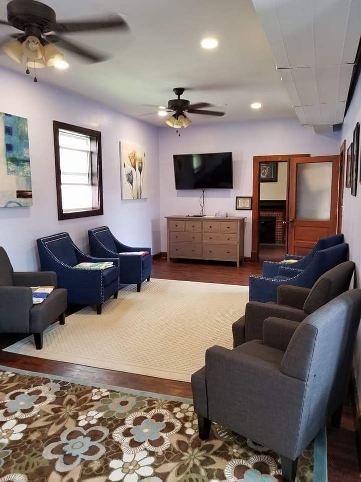 A waiting room with chairs , a television and a ceiling fan.