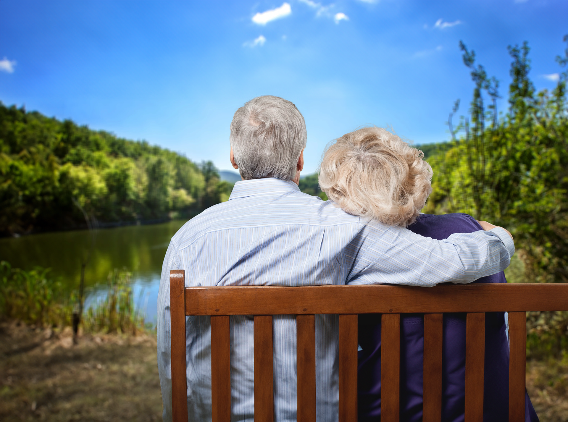 An elderly couple is sitting on a bench looking at a lake.