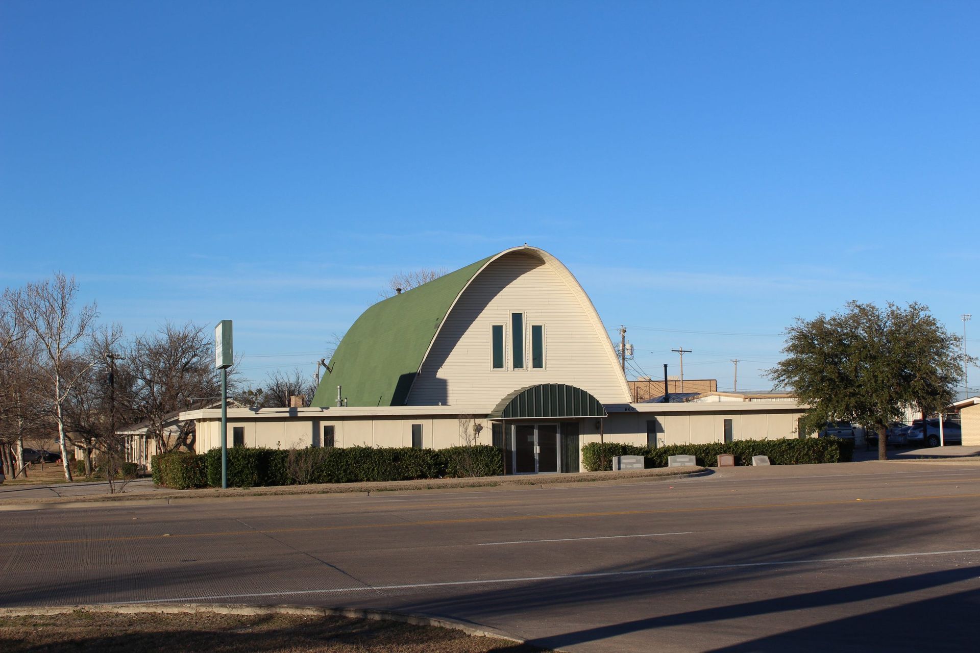 A large building with a green roof is sitting in the middle of a parking lot.