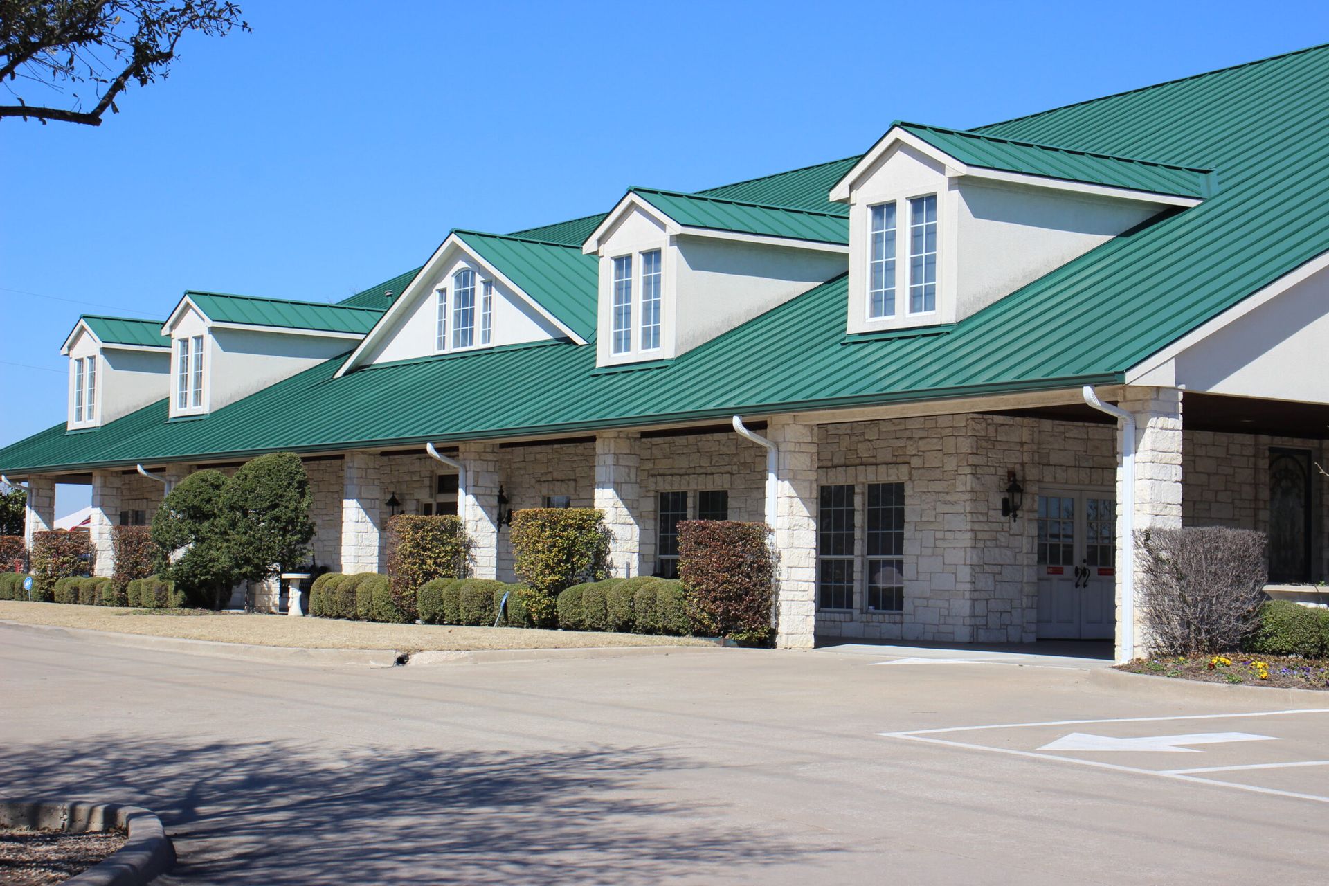 A white building with a green roof and a parking lot in front of it