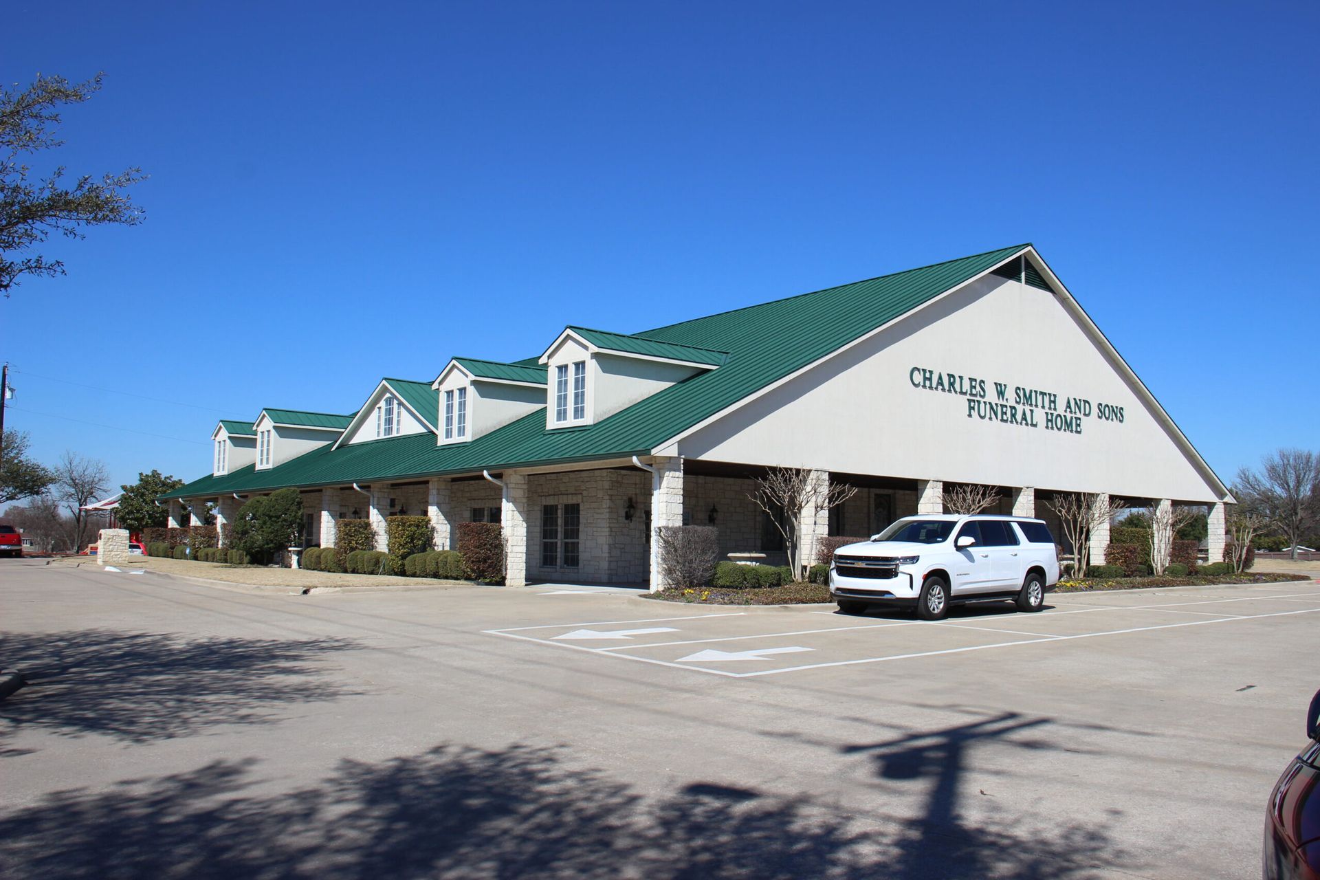 A white suv is parked in front of a building with a green roof.