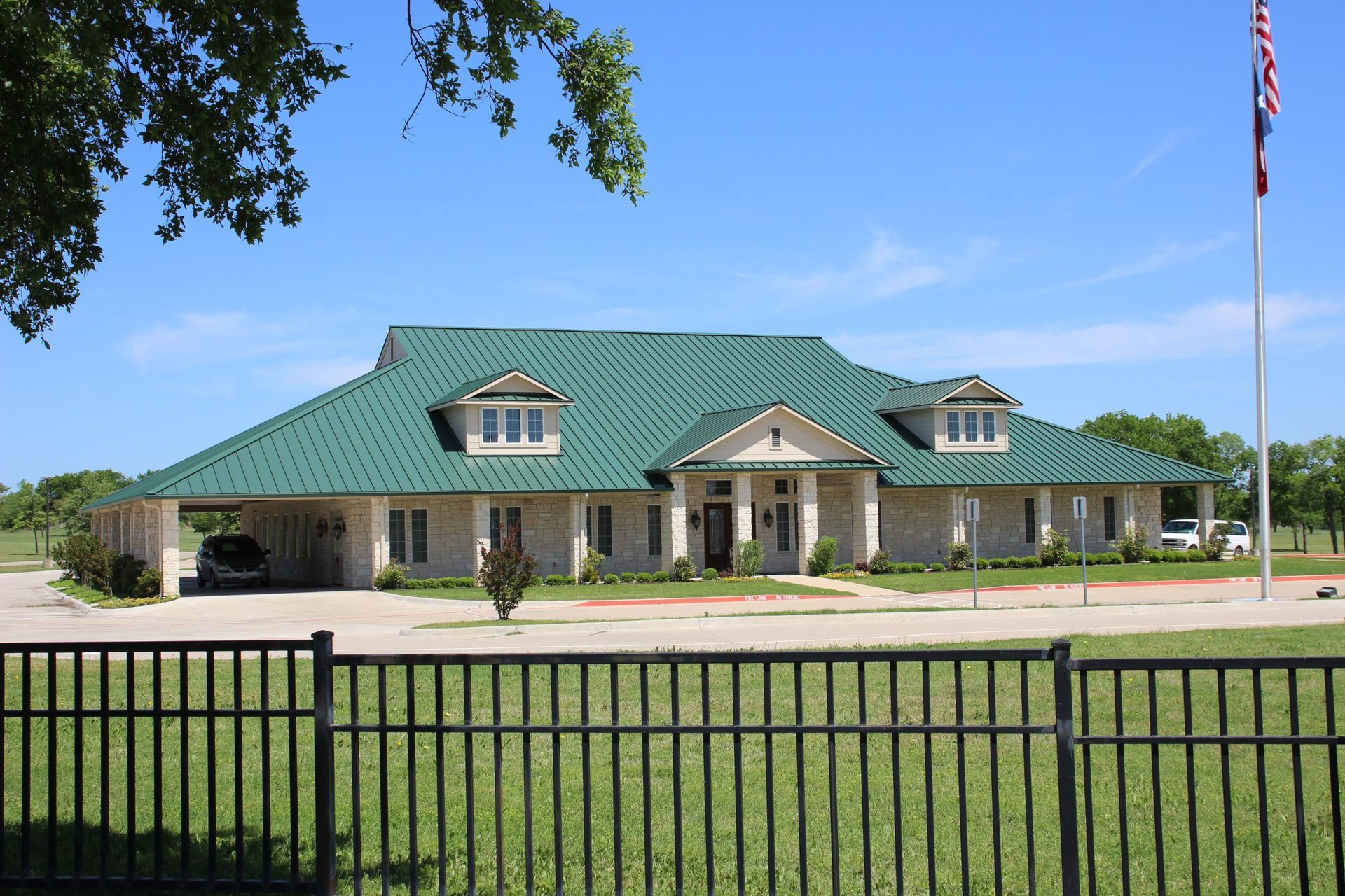 A large house with a green roof is behind a fence