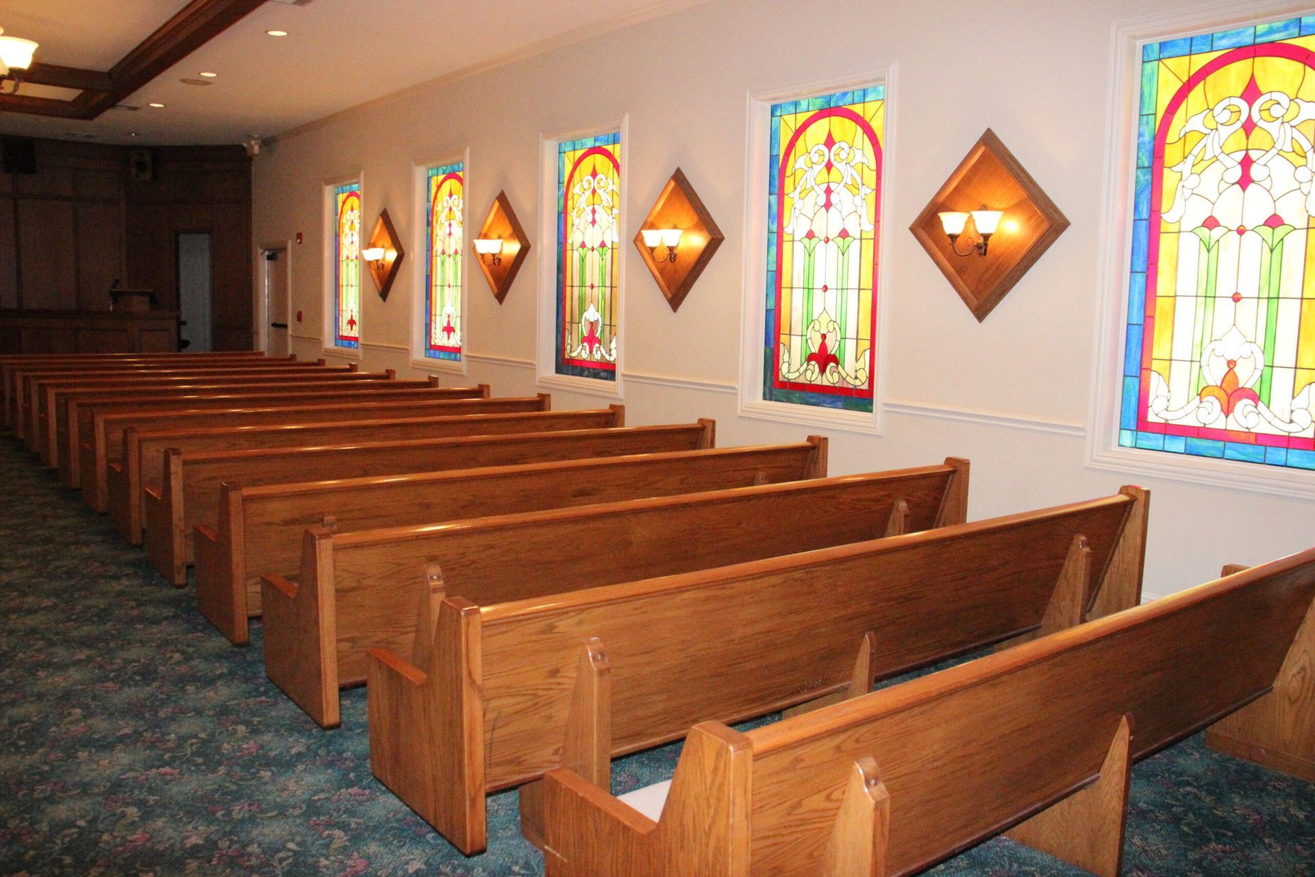 Rows of wooden benches in a church with stained glass windows